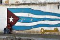 Un trabajador recostado a una pared en donde está pintada una bandera cubana