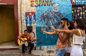 Un músico callejero toca la guitarra mientras turistas se sacan fotos en La Habana el 5 de diciembre de 2018