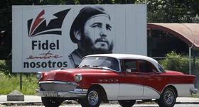 Un automóvil estadounidense de la década de 1950 pasa junto a un cartel revolucIonario en Cuba