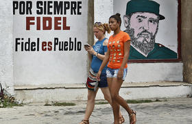 Jóvenes cubanas caminan junto a un cartel con la imagen de Fidel Castro