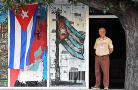Un vigilante permanece junto a la entrada de un edificio adornada con banderas de Cuba, el sábado 24 de diciembre de 2011, en La Habana. EFE