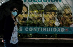 Una mujer con una mascarilla camina cerca de un cartel en La Habana