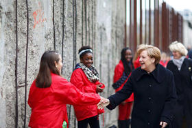 La canciller Angela Merkel saluda a unas niñas que simbolizan a aquellos que picaron el muro con martillos en el acto conmemorativo de la caída del muro en Berlín el domingo