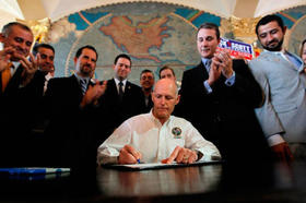 El gobernador de la Florida, Rick Scott, firma la ley en medio de los aplausos de un grupo de exiliados cubanos y dos exiliados sirios
