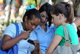 Jóvenes cubanas utilizan un teléfono celular o móvil