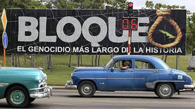 Viejos automóviles norteamericanos pasan junto a una valla que condena el embargo, en La Habana, Cuba