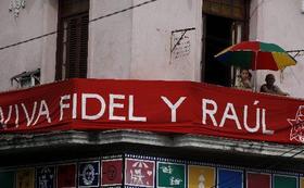 Cubanos miran hacia la calle desde un balcón con un cartel de exaltación hacia las figuras de Fidel y Raúl Castro, el 16 de abril de 2010