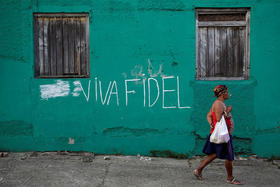 Mujer camina junto a una pared con un letrero a favor de Fidel Castro en Cuba