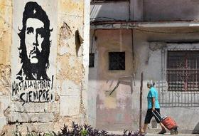Una cubana camina junto a una pared deteriorada, con un dibujo y letrero alegórico a Ernesto Che Guevara