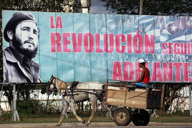 Carro tirado por un caballo pasa junto a cartel de propaganda política en Cuba