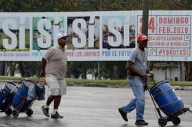 Dos hombres caminan frente a un anuncio que promueve la participación en el referendo constituyente, el 13 de febrero de 2019 en La Habana