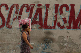 Cubana camina junto a una pared deteriorada con un lema revolucionario