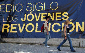 Jóvenes pasan junto a un cartel revolucionario en La Habana