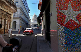 Un vehículo clásico en una calle con murales de la bandera cubana, junto al Capitolio, en La Habana