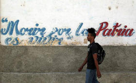 Un joven camina junto a un muro con una pintura deteriorada que muestra una estrofa del himno nacional de Cuba el miércoles 15 de abril de 2015, en una calle de La Habana