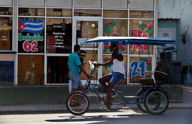 Dos personas pasan frente a una cafetería con imágenes en apoyo a la revolución cubana, en La Habana