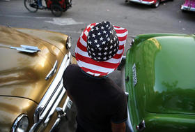 Hombre con sombrero con los colores y las estrellas de la bandera estadounidense camina entre automóviles en La Habana