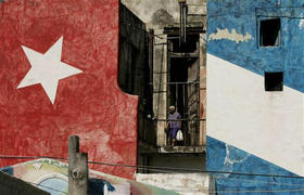 Una cubana en el balcón de un edificio pintado con los colores de la bandera cubana