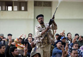 Voluntarios libios recién alistados en la resistencia rebelde gritan consignas mientras un oficial dispara su arma al aire durante el primer día de reclutamiento en la Universidad de Bengasi, Libia