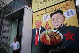 Un hombre sale de un edificio con un anuncio con las imágenes del presidente de EEUU, Donald Trump, y del gobernante norcoreano, Kim Jong-un, para publicitar el plato «Trump-Kim Chi Nasi Lemak» de un restaurante en Singapur, el 6 de junio de 2018