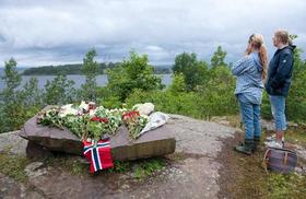 Algunas personas colocan arreglos florales en la región de Utvika, frente a la isla de Utoya (fondo), después de que el pasado viernes el autor confeso de los atentados Behring Breivik matara al menos a 93 personas, según el último recuento oficial, en dos atentados coordinados