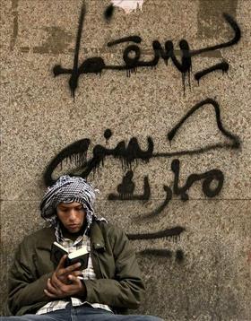 Un manifestante lee el Corán apoyado en un muro en el que se lee “Abajo Mubarak” tras los enfrentamientos en la plaza Tahrir (de la Liberación), en El Cairo, Egipto
