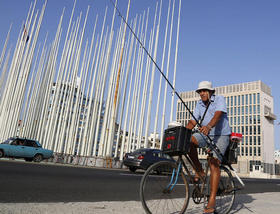 En esta foto del 8 de mayo de 2015, un pescador pedalea frente al edificio de lo que entonces era la Sección de Intereses de los Estados Unidos, atrás derecha, junto al malecón en La Habana, Cuba. Washington y La Habana inician hoy una nueva fase en sus relaciones con la reapertura de sus respectivas embajadas