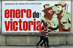 Dos cubanos pasan junto a un cartel que celebra el triunfo de la Revolución Cubana