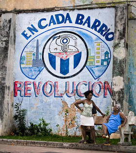 Dos mujeres conversan en La Habana ante un cartel alusivo a  los Comités de Defensa de la Revolución. (Fotografía tomada de Infolatam.)