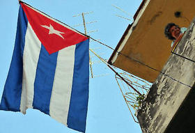 Una anciana se asoma a un deteriorado balcón en la isla, donde hay una bandera cubana