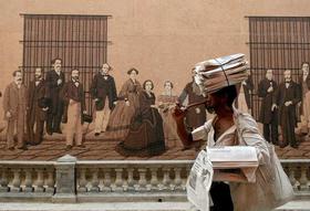 Un vendedor del diario Granma, órgano oficial del Partido Comunista de Cuba, enciende un cigarro mientras pasa frente a un mural en la ciudad de La Habana, Cuba, en esta foto de archivo de septiembre de 2006