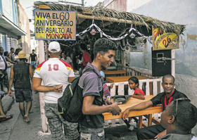 Jóvenes caminan junto a un cartel que rememora el asalto al cuartel Moncada, en Santiago de Cuba