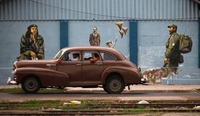Un viejo automóvil estadounidense pasa junto a un mural en Cuba, que muestra imágenes de Ernesto “Che” Guevara, José Martí y Fidel Castro